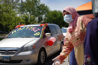 A woman wearing a mask stands next to a car decorated for Eid.