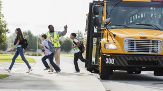 A crossing guard motions for kids getting off of a school bus to cross the street.