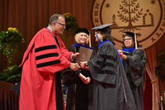 President Edward Montgomery shakes Dr. Dweepobotee Brahma's hand on the commencement stage.