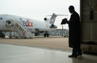 A silhouette of Dezmond Stover in front of a large FedEx plane.