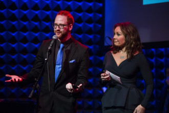 David Alpert and Vanessa Williams stand at a microphone on a stage.