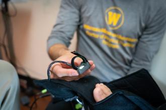 A hand holds the sensor that is placed on a patient's toe.