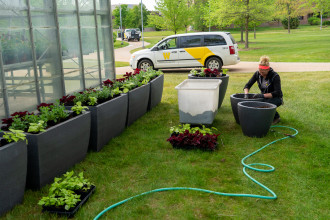 A Landscape Services crew member kneels beside a planter, adding soil for a plant.