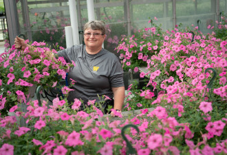 Rhonda Cosby is surrounded by baskets of pink flowers.