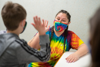 A student wearing a tie-dye t-shirt gives a high five to a child.