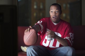 A man holding a football watches TV.