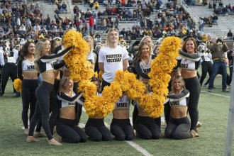 Nik McNees is surrounded by his dance teammates who are holding their pompoms in the shape of a "W."