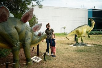 A family looks at a dinosaur statue.