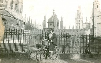 Merze Tate smiles while sitting on her bike in front of the gates of Oxford University.
