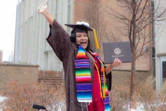 A student raises her arm in excitement while posing for a graduation photo.