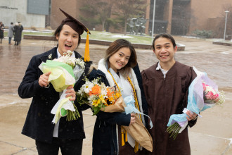 Three students in commencement regalia pose for a picture.