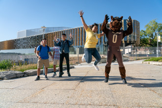 Students jump for joy next to Buster Bronco in front of the new student center.