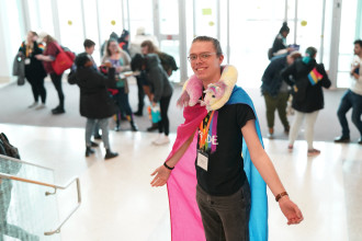 A student stands on stairs wearing the pansexual flag as a cape.