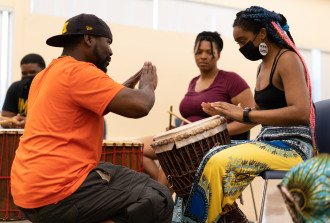 An instructor teaches students how to use an African drum.