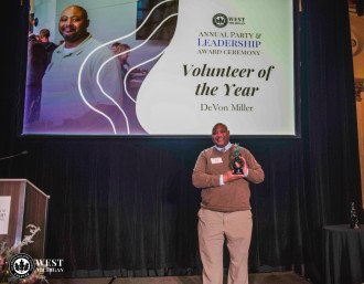 DeVon Miller holds a trophy on stage under a sign that reads, "Volunteer of the Year."