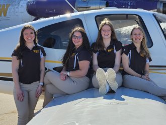 Four students pose for a photo on the wing of an airplane.