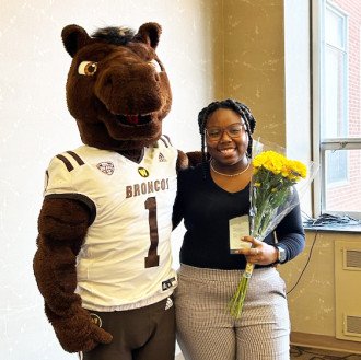 Ja'Nae Jones holds a bouquet of yellow flowers while standing next to Buster Bronco.