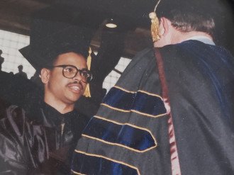 James Rhodes shakes hands with an academic official wearing full commencement regalia.