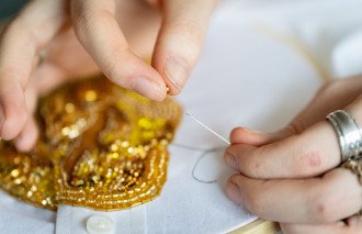 A close-up photo of hands threading a needle through a bead.