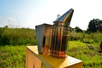 Photo of a bee smoker with a field in the background.