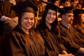 Photo of two female graduates in full regalia, seated during an WMU commencement ceremony.
