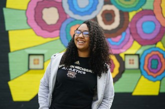 A high school student stands in front of a colorful mural at Maple Street Magnet Middle School for the Arts.
