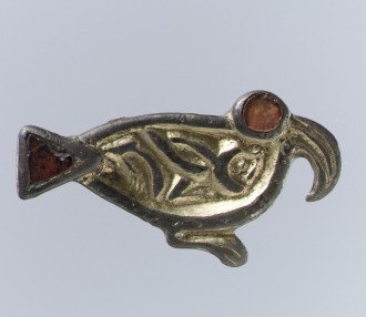 A sixth-century brooch in the shape of a bird seen from the side, with a sharply hooked beak and a large red eye, made of silver-gilt and garnets.