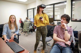 Students sitting at computers and wearing virtual reality gear and controls in a VR lab at Waldo Library.
