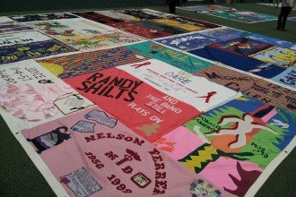 Photo of a large quilt spread on the ground with artwork and names honoring victims of AIDS.