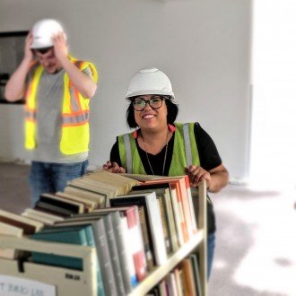 Photo of librarian Juliana Espinosa moving a cart of books with a man standing behind her.