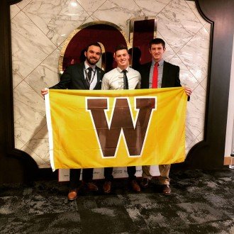 Photo of WMU students Cooper Frost, Ryan Demas and Alex McMahon holding a W flag.