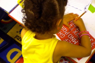 Photo of the back of a child's head who is drawing.