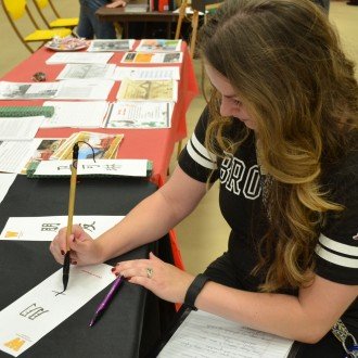 Photo of an attendee at a prior year's China Festival learning how to write in a Chinese language.