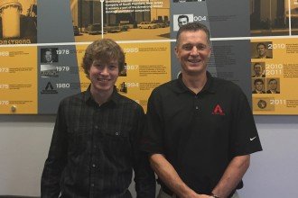 Mitchell Bingaman and his internship supervisor posing in front of a poster displaying key points in Armstrong International's history.