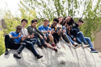 A large group of students sitting on top of one of the campus's giant boulders.