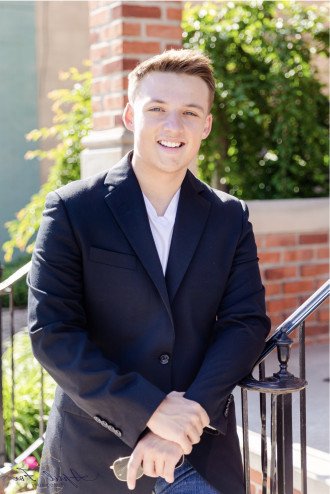 Photo of Spencer Gould in a dark blazer standing outside next to a brick wall