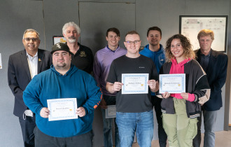 Students in one of Professor Tom Kelly's process management courses stand holding their Yellow Belt Certifications.