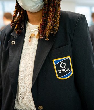Student, masked, wears a blazer with the DECA logo embroidered on the pocket.