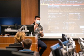 Student, masked, presents on financial topics in Greenleaf Trust Trading Room.