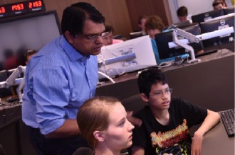 Professor talking to two campers who are working at computers.