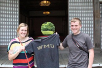 Two students hold up a WMU T-shirt outside a temple.