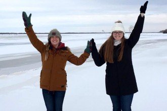 Two WMU students, Kayla Combs and Kayla Poole, pose on an iced-over lake, forming a W with their outstretched arms.