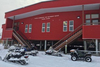 Snowmobiles sit parked outside a red school building, Kaltag Elementary and Secondary School.