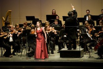  a photo of a woman in a red formal dress singing in front of an orchestra dressed in black at Western Michigan University