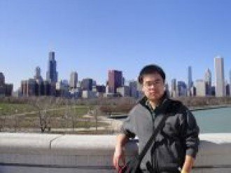 a photo of Haolai Jiang, doctoral associate for the Graduate Center for Research and Retention. Mr. Jiang is standing against a concreet wall with a sprawling cityscape behind him. Tall skyscrapers are visable, and a large body of water is to the right-hand side of the photo.