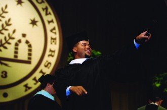 A student holds his diploma up above his head in celebration at graduation.