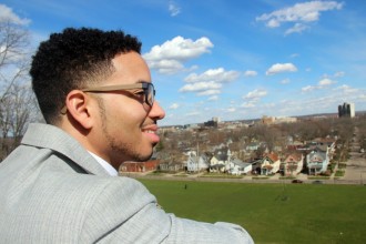 A well-dressed African-American graduate student surveys the Kalamazoo valley as it spreads out below him from his vantage point at Heritage Hall on the top of Prospect Hill. Behind him fluffy little white clouds dot the vibrant blue sky. He smiles and perhaps is looking towards the brighter future that he has earned by investing in his own graduate education at Western Michigan University.