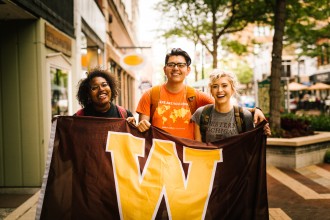 Three WMU students hold a "W" flag in downtown Kalamazoo.