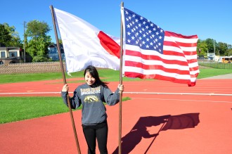 Japanese exchange student in a WMU sweatshirt smiles while holding Japanese and U.S. American flag.