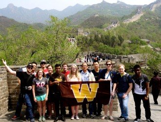 Group of WMU students with the WMU flag standing on the Great Wall of China.